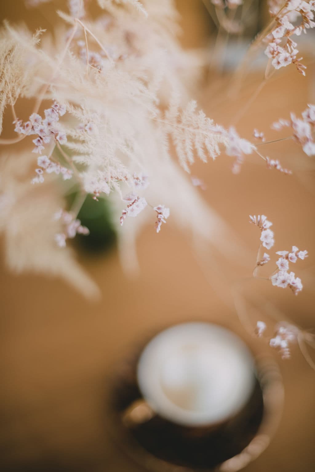 Pampas grass en gedroogde bloemen boven een espressokopje op een warme aardetint tafel — sfeerbeeld van de Moonrebel werkplek